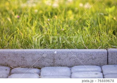 Closeup of pavement curb with green grass lawn behind. Closeup of pavement curb with green grass lawn behind. 76889678