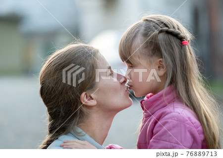 Happy mother and child daughter hugging together and kissing outdoors. Happy mother and child daughter hugging together and kissing outdoors. 76889713