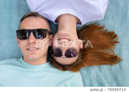 Young teenage couple in sunglasses laying together on blue cloth enjoying love relations. Young teenage couple in sunglasses laying together on blue cloth enjoying love relations. 76889714