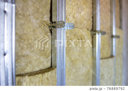 Wall of a room under renovation with mineral rock wool insulation and metal frame prepared for drywall plates. 76889792