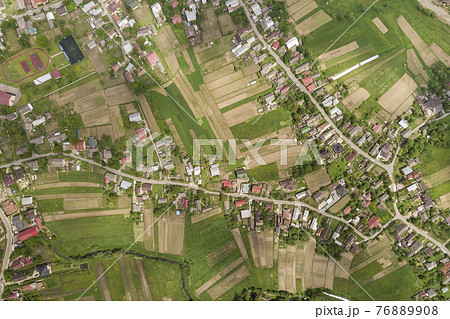Top down aerial view of town or village with rows of buildings and curvy streets between green fields in summer. Countryside landscape from above. 76889908
