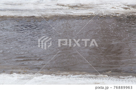 A deep puddle of ice and snow along the edges on the road in the city. 76889963