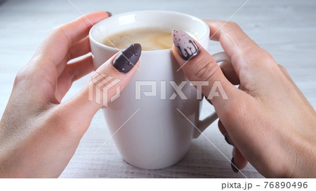 Beautiful manicured nails in the form of chocolate candies on female hands close-up and a cup of 76890496