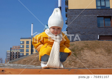 Beautiful baby in an orange coat and white hat and scarf Beautiful baby in an orange coat and white hat and scarf 76891107
