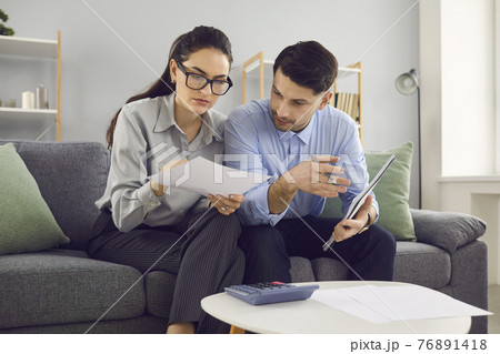 Married couple analyzes and calculates their financial accounts while sitting on the couch. Married couple analyzes and calculates their financial accounts while sitting on the couch. 76891418