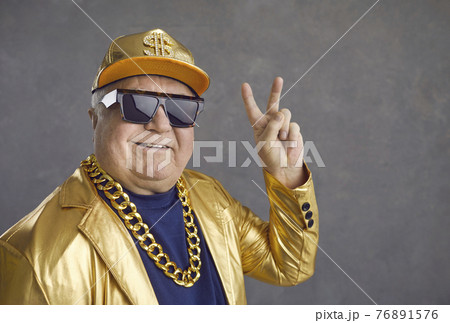 Funny and cheerful senior man in luxury clothes showing v-sign on gray background. 76891576