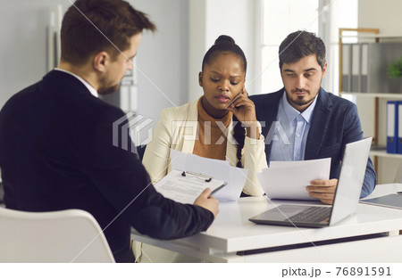 Married couple carefully examines an important contract while sitting in a meeting at a bank office. Married couple carefully examines an important contract while sitting in a meeting at a bank office. 76891591