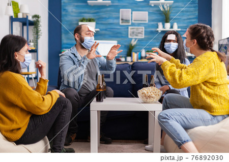 Happy cheerful multi ethnic friends with face mask playing game 76892030