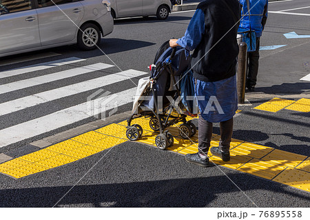 横断歩道を渡ろうとして信号が変わるのを待っている赤ちゃん連れの母親の写真素材