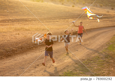 three joyful children, boys, run along a dirt road and launch toy airplanes and a kite, in backlight, concept three joyful children, boys, run along a dirt road and launch toy airplanes and a kite, in backlight, concept 76900292