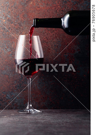 Red wine is poured from a bottle into a wine glass on rusty brown background. 76905678