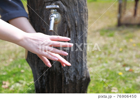 春らしい暖かい日の公園で散歩の途中で手を洗う女性 76906450