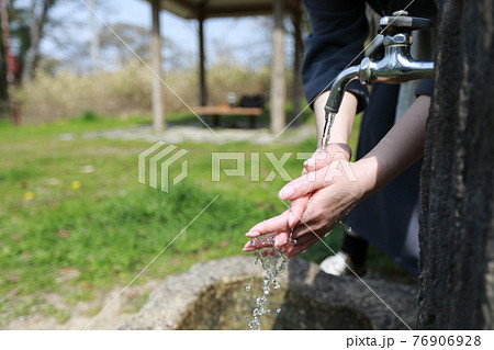 春らしい暖かい日の公園で散歩の途中で手を洗う女性 76906928