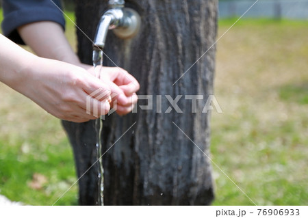 春らしい暖かい日の公園で散歩の途中で手を洗う女性 76906933
