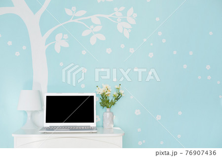Shot of modern laptop computer with blank screen for your text on white table, lamp and flowers against light blue wall decorated with white tree print. Technology and furniture concept 76907436