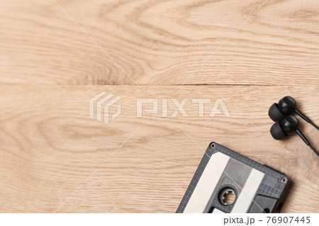 Shot of audio cassette and earphones in right corner over wooden surface. Music and revolution. Musical objects. Selective focus. Vintage style Shot of audio cassette and earphones in right corner over wooden surface. Music and revolution. Musical objects. Selective focus. Vintage style 76907445