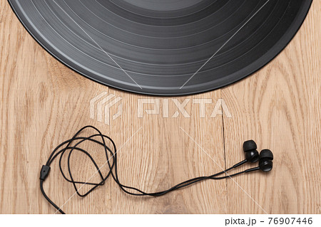 Vinyl record and contemporary earphones on wooden flat background. Music and revolution concept. Top view. Vinyl record and contemporary earphones on wooden flat background. Music and revolution concept. Top view. 76907446