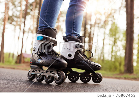Close up picture of rollerblades, unknown person wearing rollerskates to spend time actively, black rollerblades with wheels being on road in fresh air, trying new purchase. Rollerskating concept. 76907455