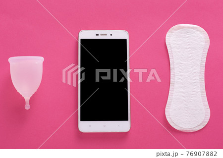 Image of clean menstrual cup, smartphone and sanitary pad lying nearby isolated over pink background, choice between reusable product and disposable one, device app. Flat lay composition concept Image of clean menstrual cup, smartphone and sanitary pad lying nearby isolated over pink background, choice between reusable product and disposable one, device app. Flat lay composition concept 76907882