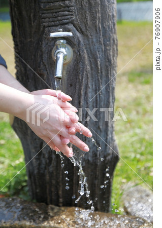 春らしい暖かい日の公園で散歩の途中で手を洗う女性 76907906