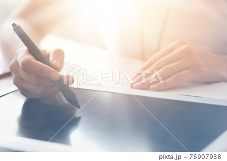 Female graphic designer or photographer working in office, using tablet pen, doing new project via tablet with blank screen, woman sitting at table and working online, holding stylus in hands. 76907938