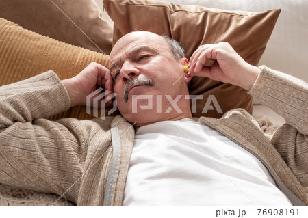 Senior stressed man holding a yellow earplug trying to sleep having insomnia Senior stressed man holding a yellow earplug trying to sleep having insomnia 76908191