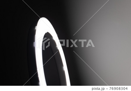 Large LED ring light in a studio room against empty walls side view and the very dark to bright light gradient wall effect. 76908304