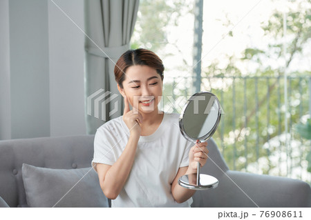 Beauty skin care. Young beautiful asian girl touching her face before the mirror, enjoying her clean skin. 76908611