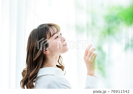 カーテンを開けて日差しを浴びる若い女性 76911542