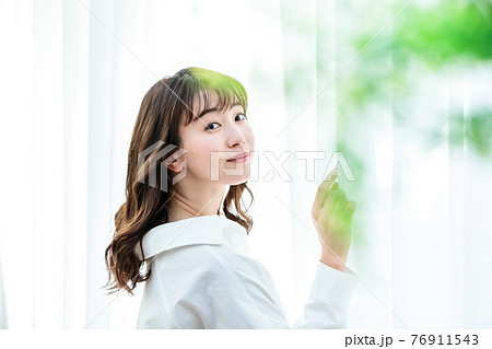 カーテンを開けて日差しを浴びる若い女性 76911543