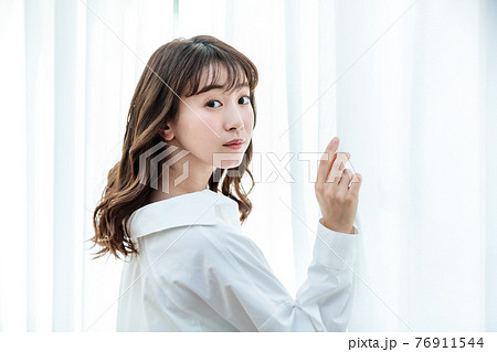 カーテンを開けて日差しを浴びる若い女性 76911544