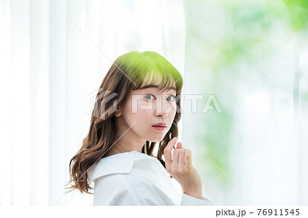 カーテンを開けて日差しを浴びる若い女性 76911545