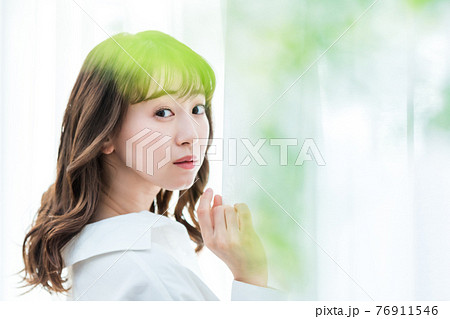 カーテンを開けて日差しを浴びる若い女性 76911546