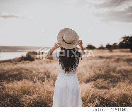 Brunette girl in a white dress with curly hair puts on a boatman hat Brunette girl in a white dress with curly hair puts on a boatman hat 76911605