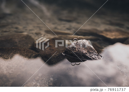 engagement simple gold rings stand on a gray stone in the middle of clear transparent crystal water 76911737