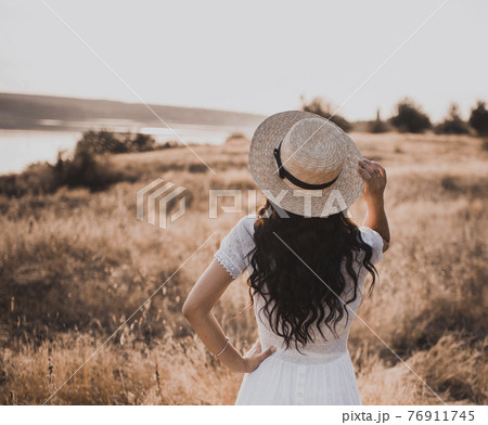Brunette girl in a white dress with curly hair puts on a boatman hat Brunette girl in a white dress with curly hair puts on a boatman hat 76911745
