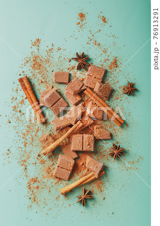 Dark chocolate slices with cinnamon and spices on a pastel green background. Dark chocolate slices with cinnamon and spices on a pastel green background. 76913291