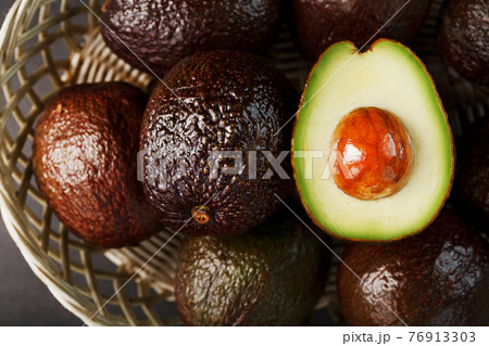 Ripe avocados in a basket on a black table, with a cut fruit and a stone. 76913303