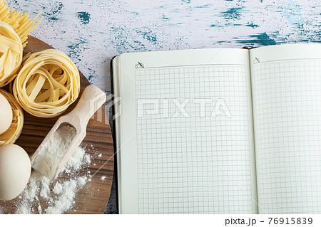 Tagliatelle with egg and flour on wooden board and notebook Tagliatelle with egg and flour on wooden board and notebook 76915839