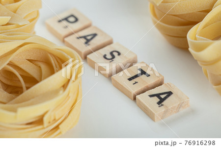 Tagliatelle nests on white surface with wooden letters 76916298