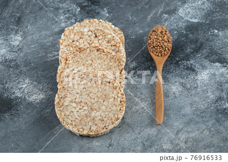Puffed crispbread and wooden spoon of raw buckwheat on marble surface Puffed crispbread and wooden spoon of raw buckwheat on marble surface 76916533