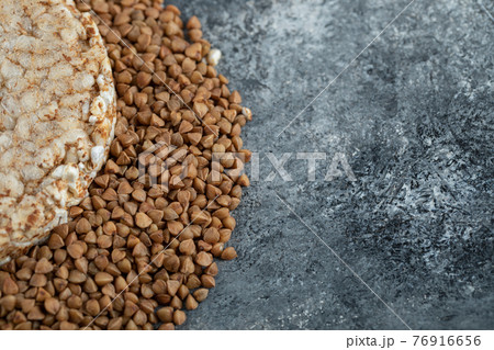 Single rice cake and uncooked buckwheat on marble surface Single rice cake and uncooked buckwheat on marble surface 76916656