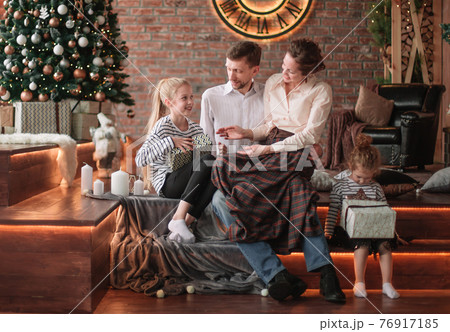 parents with their young children sitting in the living room decorated for Christmas parents with their young children sitting in the living room decorated for Christmas 76917185