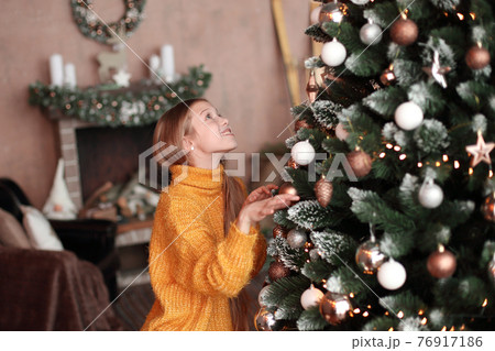 smiling teen girl decorating Christmas tree in cozy living room smiling teen girl decorating Christmas tree in cozy living room 76917186