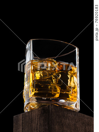 Luxury crystal glass with ice cubes of scotch whiskey on top of wooden box and black. 76920183