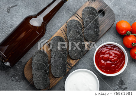 Black crispy potato chips , with dipping sauces tomato dip sour cream, and bottle of beer , on gray stone background, top view flat lay Black crispy potato chips , with dipping sauces tomato dip sour cream, and bottle of beer , on gray stone background, top view flat lay 76931981