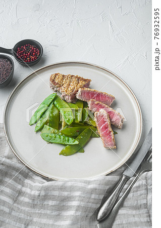 Sesame tuna steak grilled with spring onions and sugar snap peas, on plate, on white stone background Sesame tuna steak grilled with spring onions and sugar snap peas, on plate, on white stone background 76932595