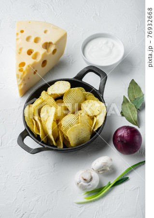 Crispy potato chips. Slices of potato, roasted with sea salt with Cheese and Onion , with dipping sauces tomato dip sour cream, on white stone surface 76932668