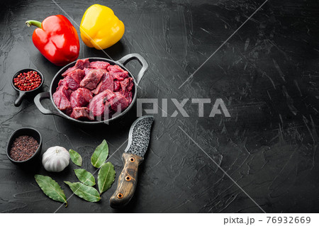 Raw meat diced for stew with sweet bell pepper, in cast iron frying pan, on black stone background, with copy space for text 76932669