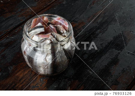 Salted anchovy fillets, in glass jar, on old dark wooden table background., with copyspace and space for text Salted anchovy fillets, in glass jar, on old dark wooden table background., with copyspace and space for text 76933126